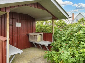 A wooden structure with a bench and a table, surrounded by greenery.