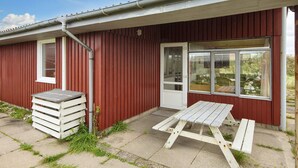 A red building with a white door and windows, a concrete patio, and a wooden picnic table. - 10 Person Holiday Home in Harboore (Harboore)