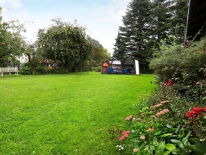 A grassy outdoor area with a bench, a table with chairs, and a small structure with a roof. - Cozy Holiday Home in Syddanmark near Sea (Aeroskobing)