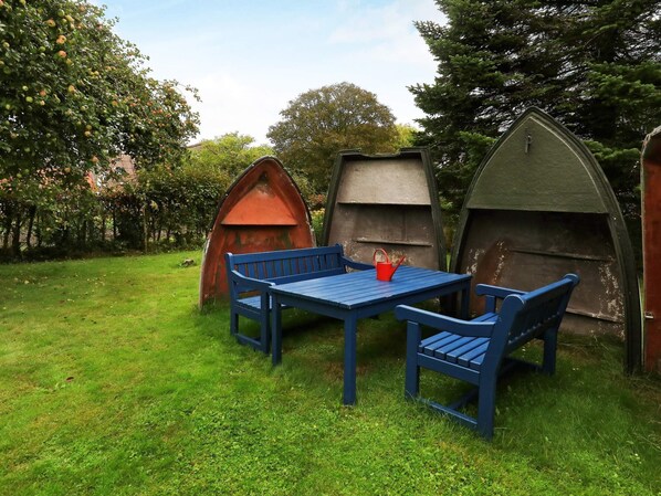 A garden with a blue table and chairs, surrounded by green grass and trees.