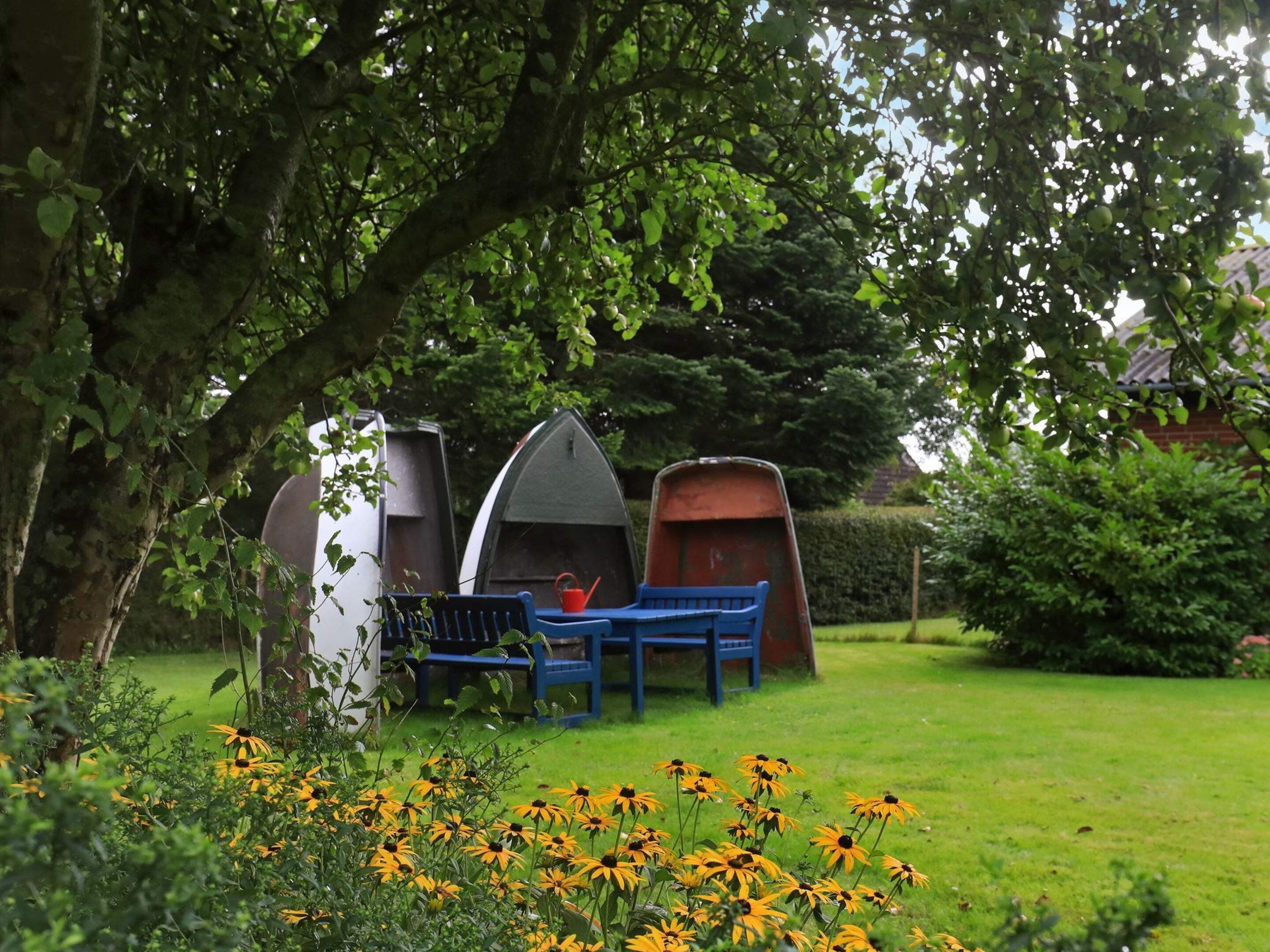 A garden with a bench, two small boats, and yellow flowers.