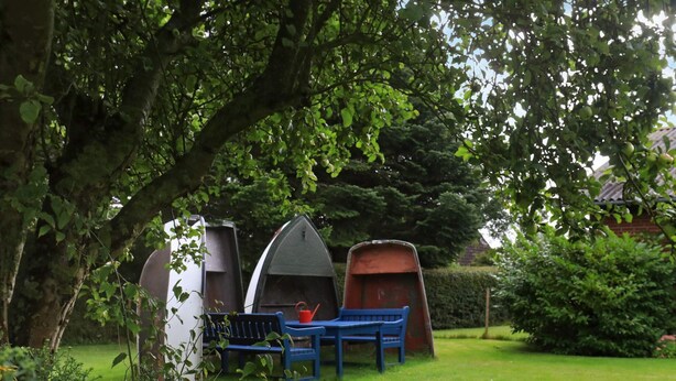 A garden with a bench, two small boats, and yellow flowers. - Cozy Holiday Home in Syddanmark near Sea (Aeroskobing)