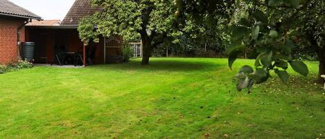 A well-maintained grassy yard with a brick building, a tree, and a metal gate.