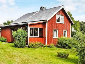 A red wooden house with a sloped roof, a front porch, and a well-maintained lawn. - 6 Person Holiday Home in Bengtsfors (Bengtsfors)