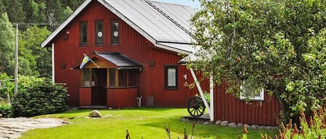 A red wooden house with a sloped roof, a porch, and a flag.