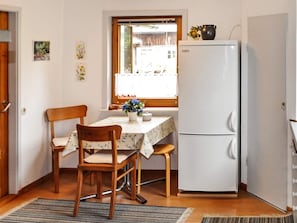 Una cocina compacta con un refrigerador blanco, sillas de madera, una mesa con mantel floreado y una ventana con vistas al exterior.