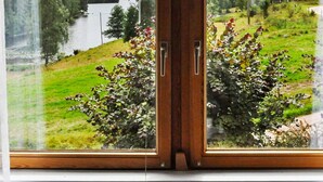 Ein Fenster mit Blick auf einen See, Grünflächen und ein Gebäude in der Ferne.