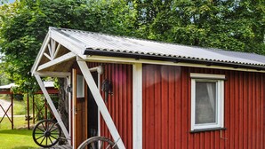 Ein rotes Holzgebäude mit weißer Tür und Fenster, einer Holzrampe und einem großen Rad.