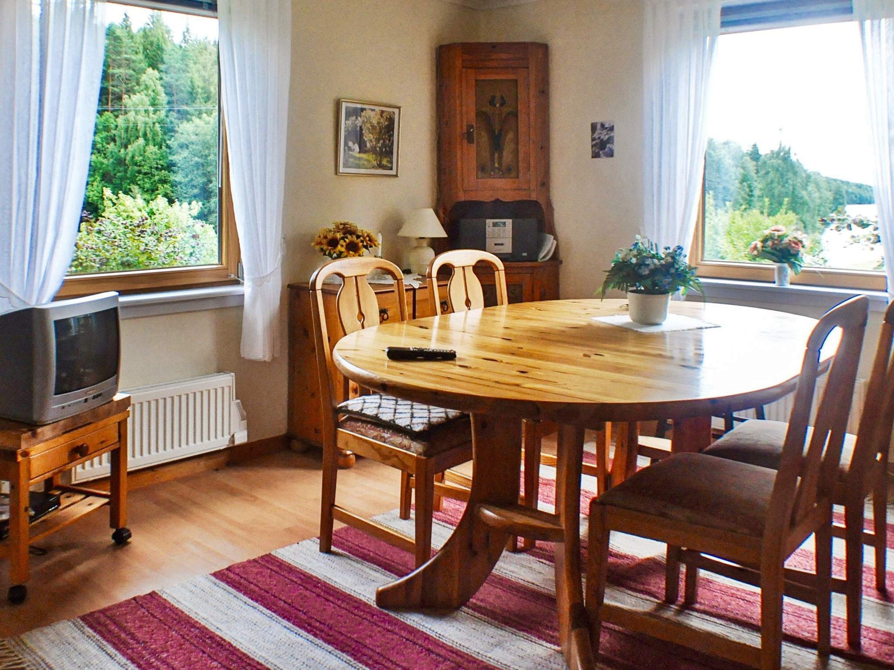 A dining area with a round wooden table, chairs, a television on a stand, and a radiator.