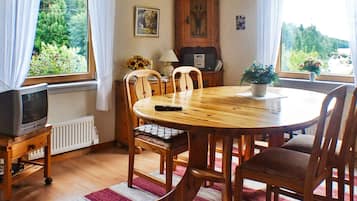 Un comedor con una mesa redonda de madera, sillas, un televisor sobre un mueble bajo y un radiador.