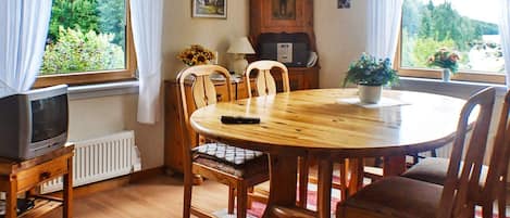 A dining area with a round wooden table, chairs, a television on a stand, and a radiator.
