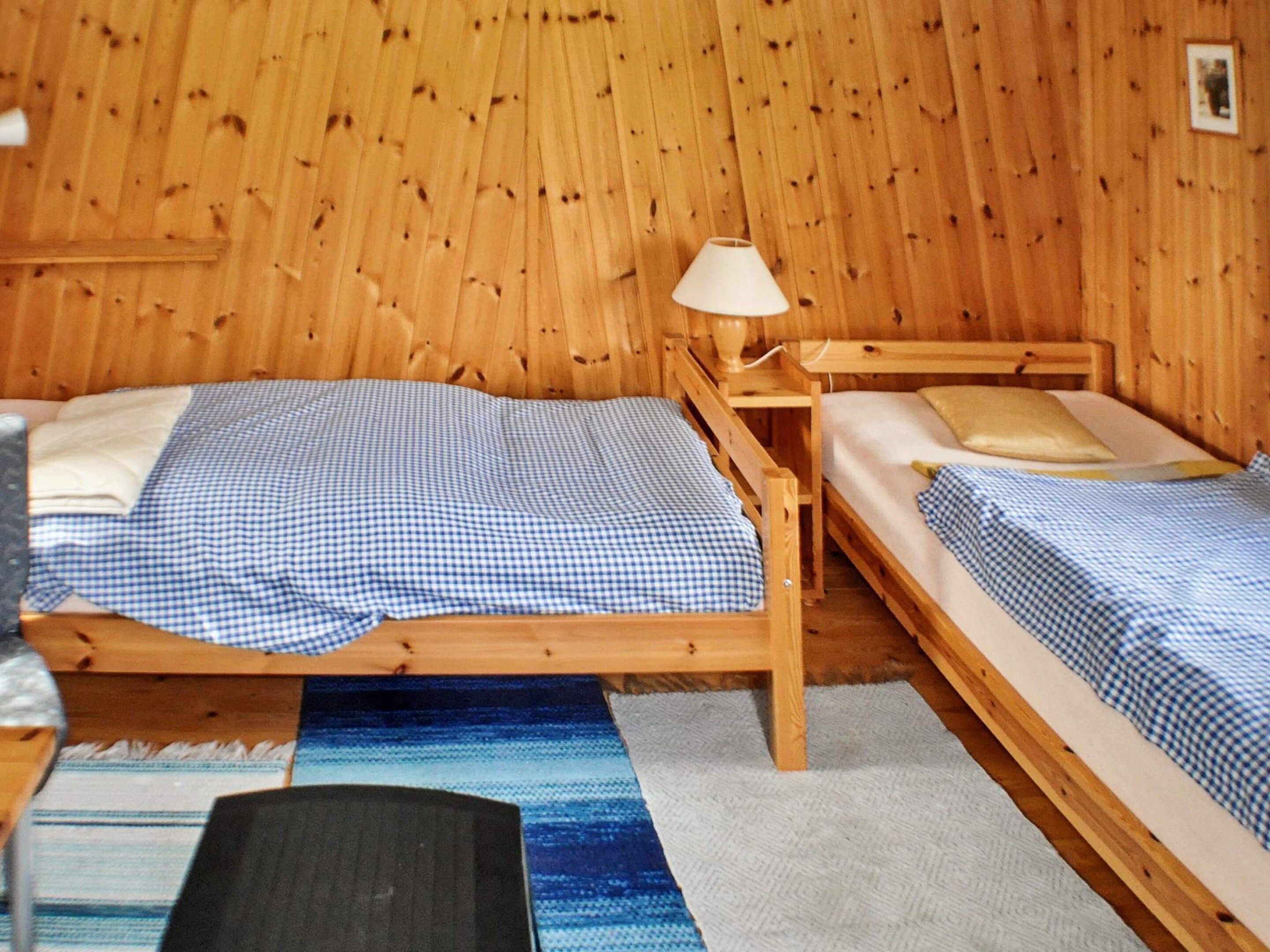 Una habitación de madera con dos camas, una lámpara y una mesita.