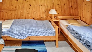 Una habitación de madera con dos camas, una lámpara y una mesita.