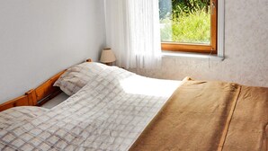 Ein Bett mit einem karierten Überwurf und einer braunen Decke, eine Nachttischlampe und ein Fenster mit Blick auf Grünflächen.