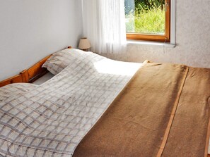 A bed with a plaid bedspread and a brown blanket, a bedside lamp, and a window with a view of greenery. - 6 Person Holiday Home in Bengtsfors (Bengtsfors)