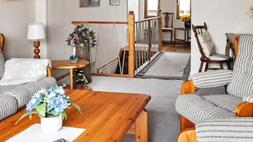 Una sala de estar con una mesa de centro de madera, sillones a rayas, un sofá, una pequeña mesa con un florero y un control remoto.