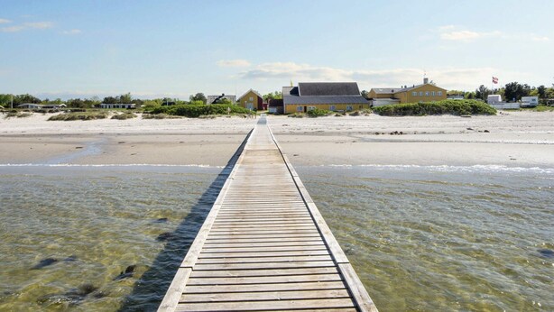 A wooden pier extending into a beach with houses in the background. - Refined Holiday Home in Glesborg near Sea (Glesborg)