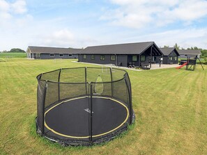 A trampoline in a grassy area with a building in the background. - 5 Star Holiday Home in Stege (Stege)