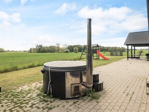 A hot tub with a chimney, a children's play structure, and a barbecue area in a backyard setting. - 5 Star Holiday Home in Stege (Stege)