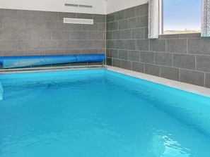 A swimming pool with a blue tint, surrounded by grey tiled walls, and a window on the right side. - 5 Star Holiday Home in Stege (Stege)