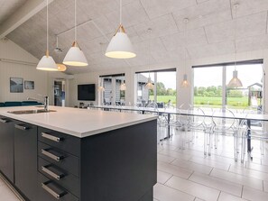 Een moderne keuken met een groot eiland, roestvrijstalen apparatuur en hanglampen.