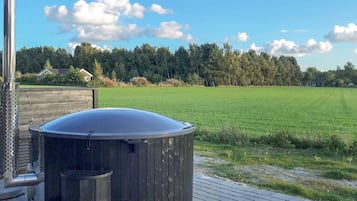 Ett bubbelbad på ett trädäck med en gräsyta och träd i bakgrunden.