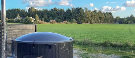 Un bain à remous sur une terrasse en bois, avec un champ verdoyant et des arbres en arrière-plan.