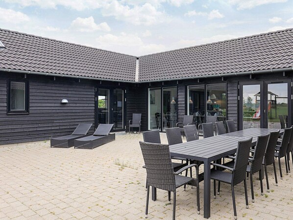 An outdoor patio with a table and chairs, a covered seating area, and a building with a tiled roof.