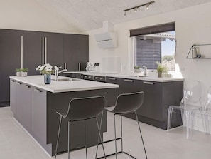 A modern kitchen with a central island, bar stools, and a window with blinds.