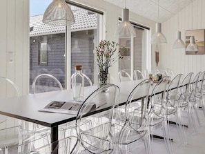 Un comedor moderno con una mesa larga, sillas transparentes y lámparas colgantes.