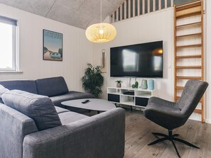 A modern living room with a grey sofa, a coffee table, a TV on the wall, and a wooden ladder.
