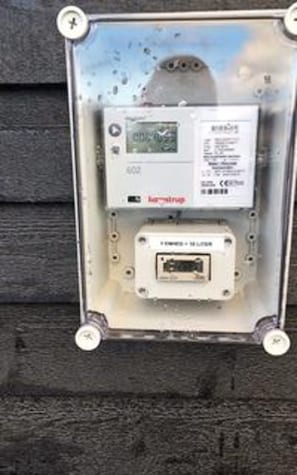 A utility meter box mounted on a wall with a digital display and a smaller device below it.