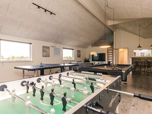 A room with a foosball table, pool table, and a bar area with stools.