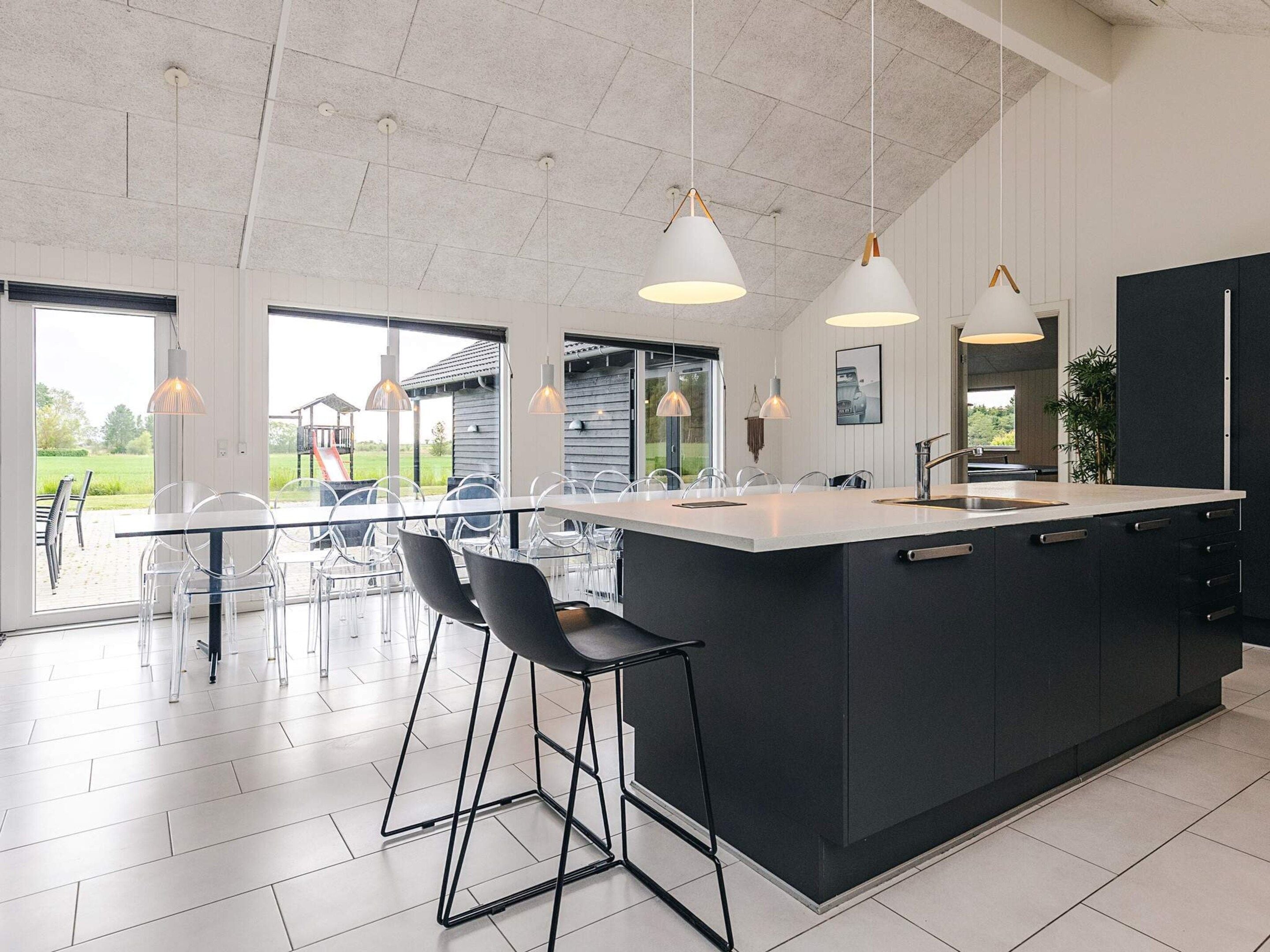 Une cuisine moderne dotée d’un grand îlot central, de luminaires suspendus et offrant une vue sur l’extérieur.