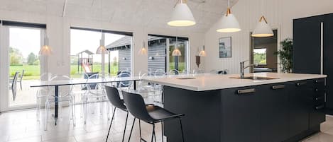 Cozinha moderna com uma ilha grande, luminárias pendentes e vista para o exterior.