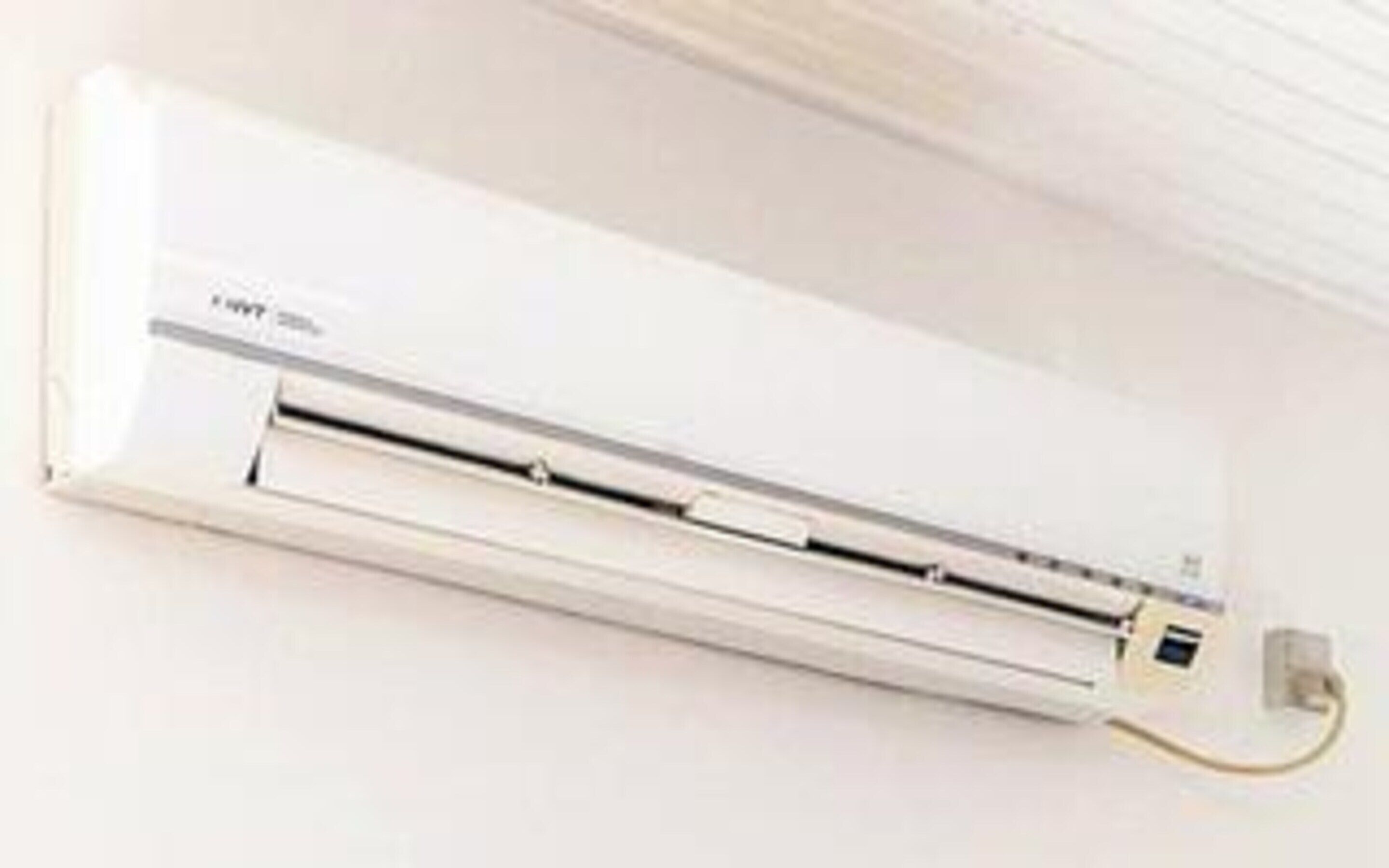 A white wall-mounted air conditioning unit with a control panel and a power cord.