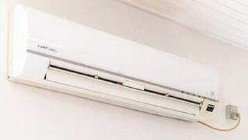 A white wall-mounted air conditioning unit with a control panel and a power cord.