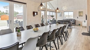 A spacious dining area with a long table, multiple chairs, pendant lighting, and a view of the outdoors. - Luxury Retreat in Albaek (Aalbaek)