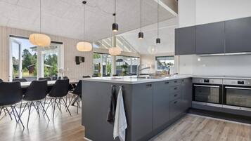 Et moderne køkken med en stor ø, indbyggede apparater og hængende lamper.