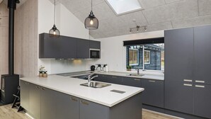 A modern kitchen with a central island, dark cabinetry, and pendant lighting. - Luxury Retreat in Albaek (Aalbaek)