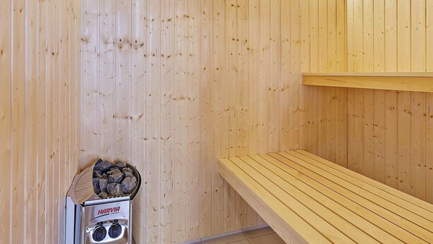 A sauna room with wooden walls, a bench, and a sauna heater. - Luxury Retreat in Albaek (Aalbaek)