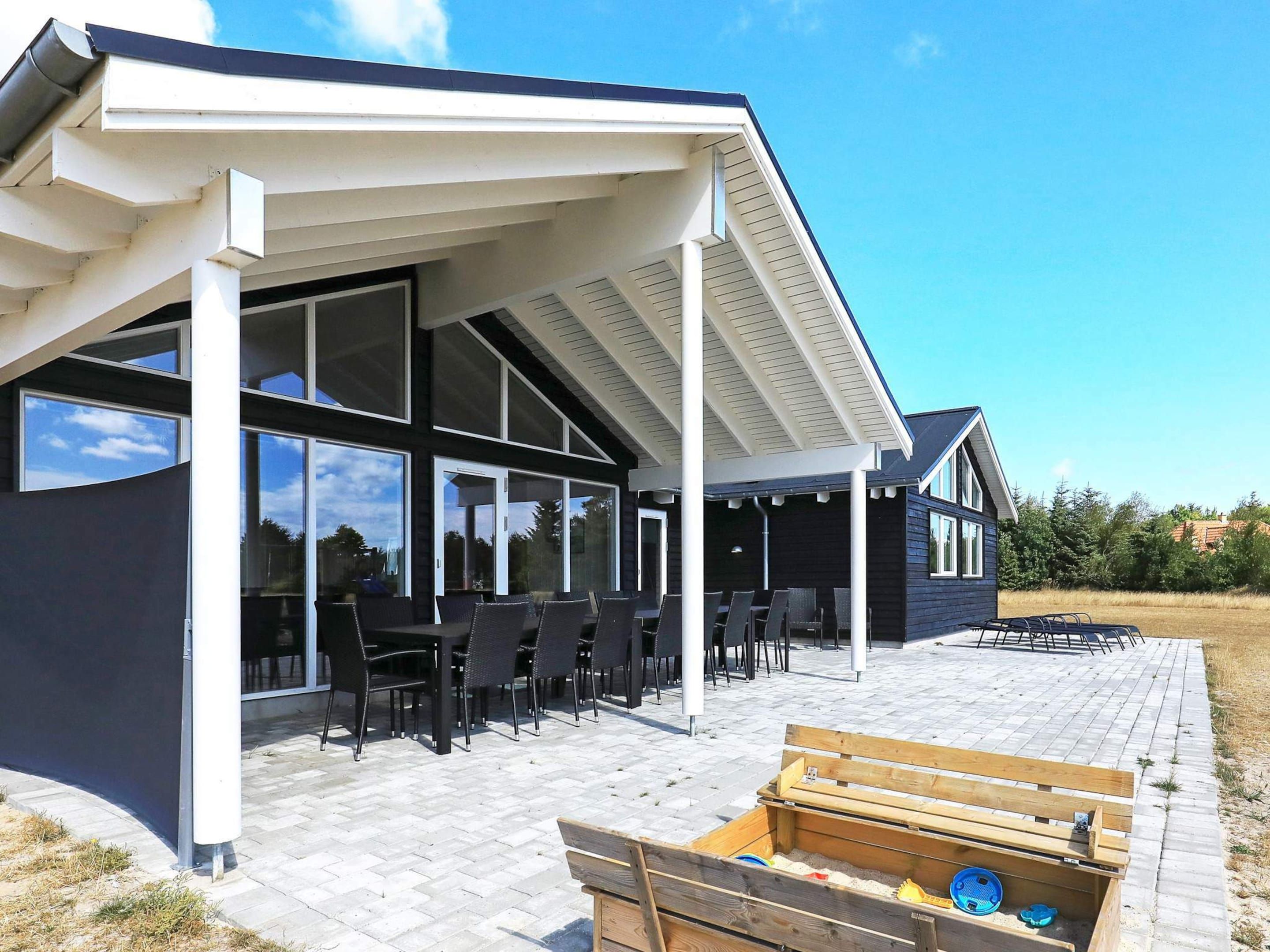 Et moderne hus med en overdækket terrasse, store vinduer og udendørs møbler.