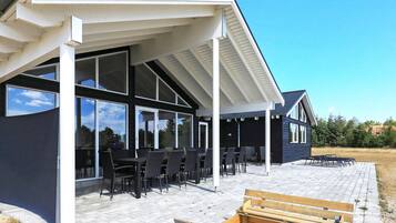 Et moderne hus med en overdækket terrasse, store vinduer og udendørs møbler.