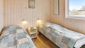 A room with two single beds, a small bedside table with a book, a framed picture on the wall, and a window with a view of the outdoors. - Luxury Retreat in Albaek (Aalbaek)