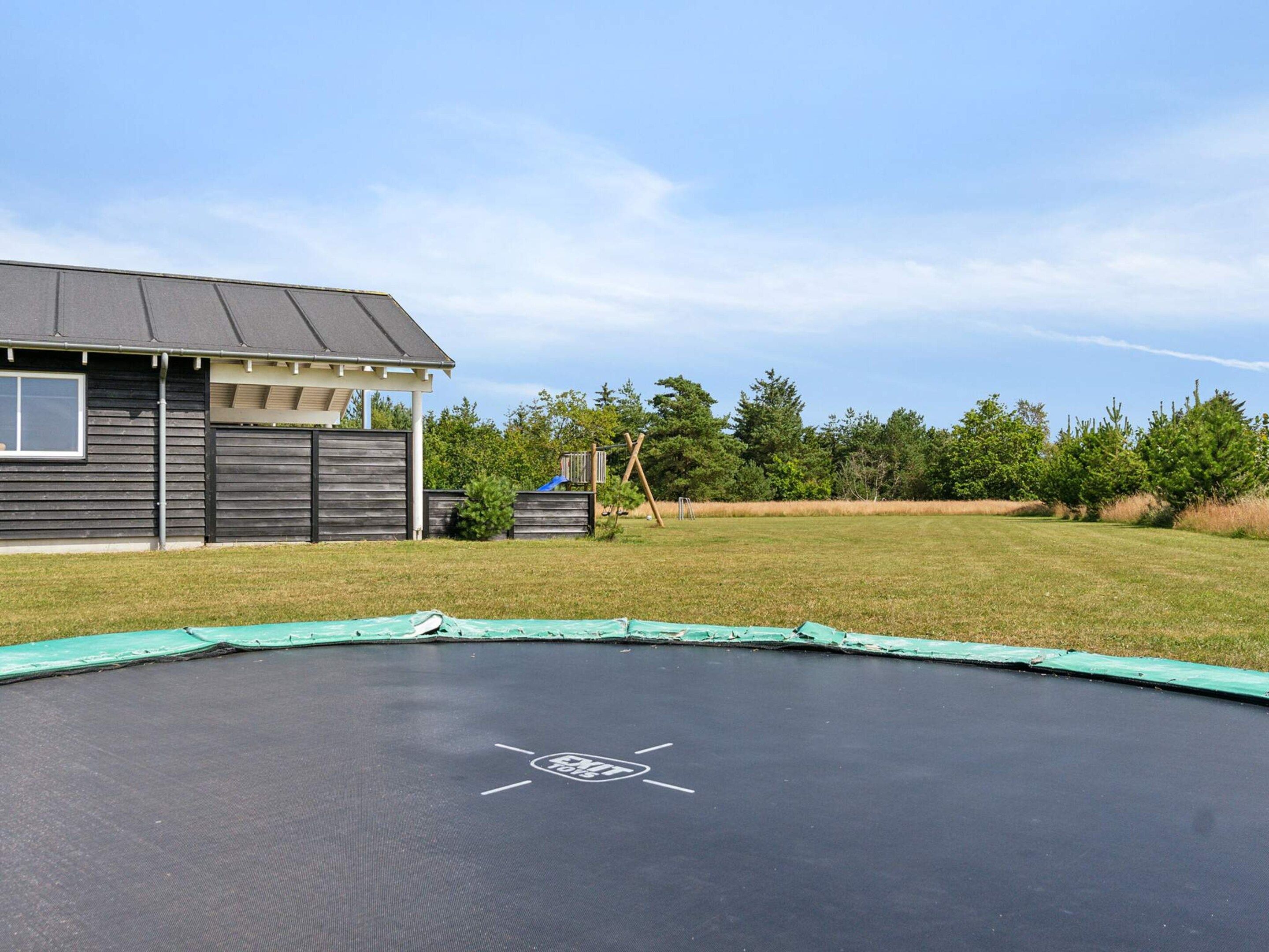 A residential backyard with a trampoline, a wooden house, and a fenced yard.