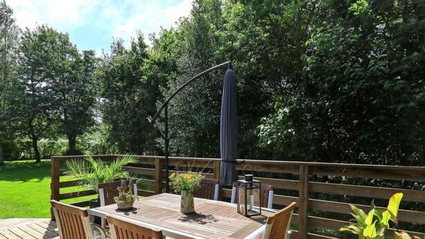 Una terraza al aire libre con una mesa y sillas de madera, rodeada por una barandilla de madera.