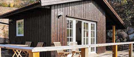 A wooden cabin with a deck, large windows, and a stone wall.