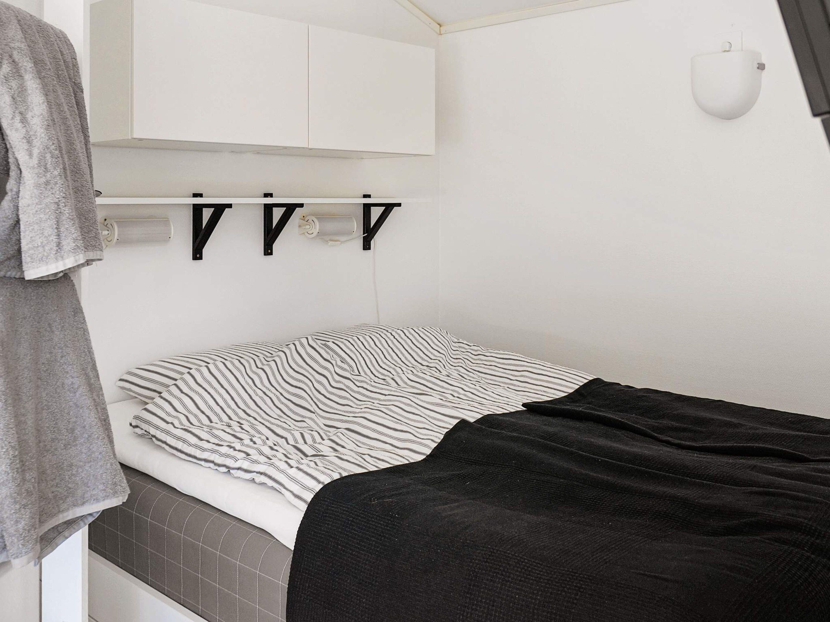 A compact bedroom with a bed, a towel, a white cabinet, and a wall-mounted light fixture.