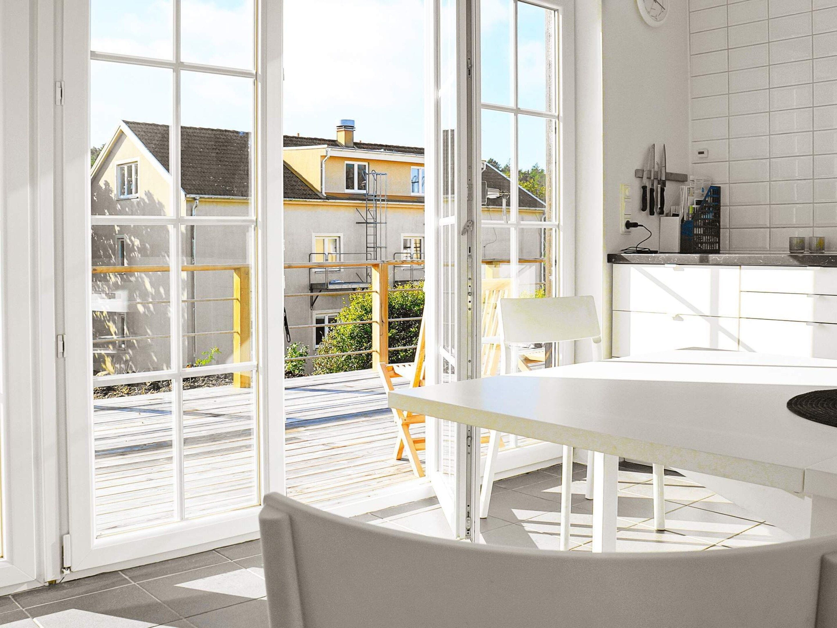 A modern kitchen with white cabinets, a dining table, and a view of neighboring houses through large glass doors.