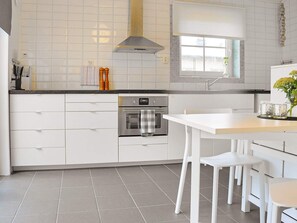 A modern kitchen with white cabinetry, a stainless steel oven, and a window with blinds.